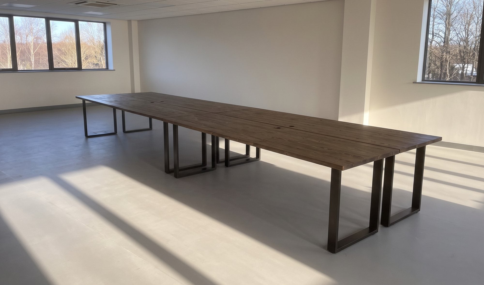 A bank of dark solid wood desks in a bright open-plan office